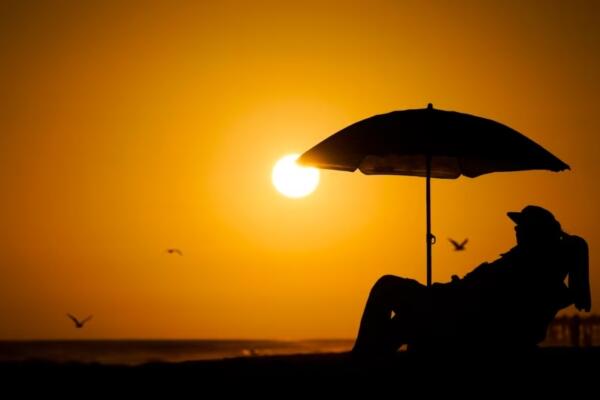  Una persona descansa bajo uns sombrilla de playa a la puesta del sol el 12 de septiembre de 2023 en Newport Beach, California, en uno de los veranos más calientes en la zona. Foto: fuente externa.