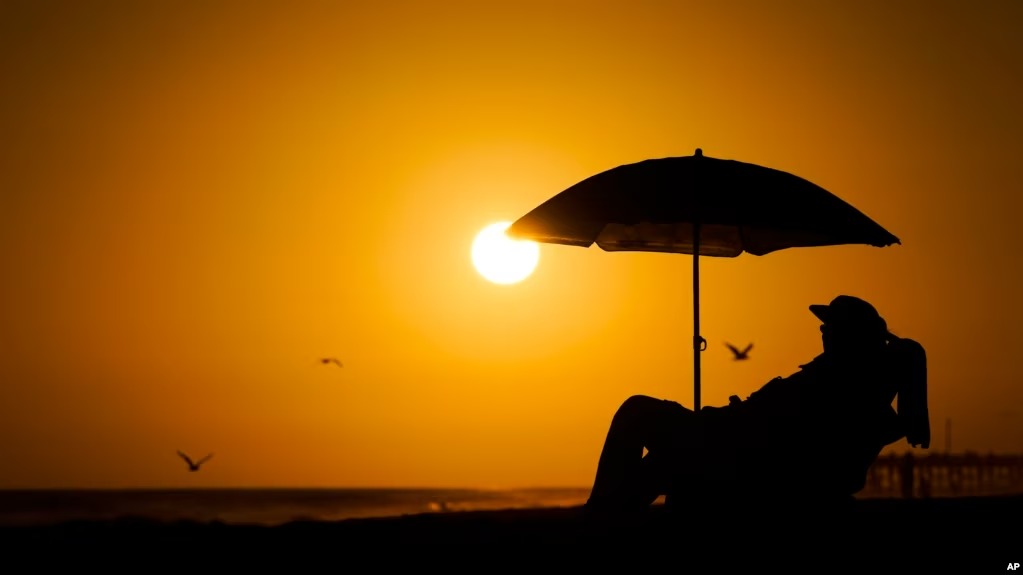 Una persona descansa bajo uns sombrilla de playa a la puesta del sol el 12 de septiembre de 2023 en Newport Beach, California, en uno de los veranos más calientes en la zona. Foto: fuente externa.