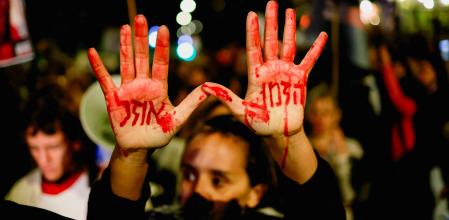 Un manifestante levanta sus manos pintadas de rojo con el mensaje 