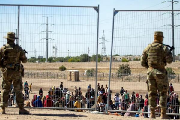 Migrantes esperan en fila junto a la valla fronteriza bajo la vigilancia de la Guardia Nacional de Texas para ingresar a El Paso, Texas. Foto: fuente externa.