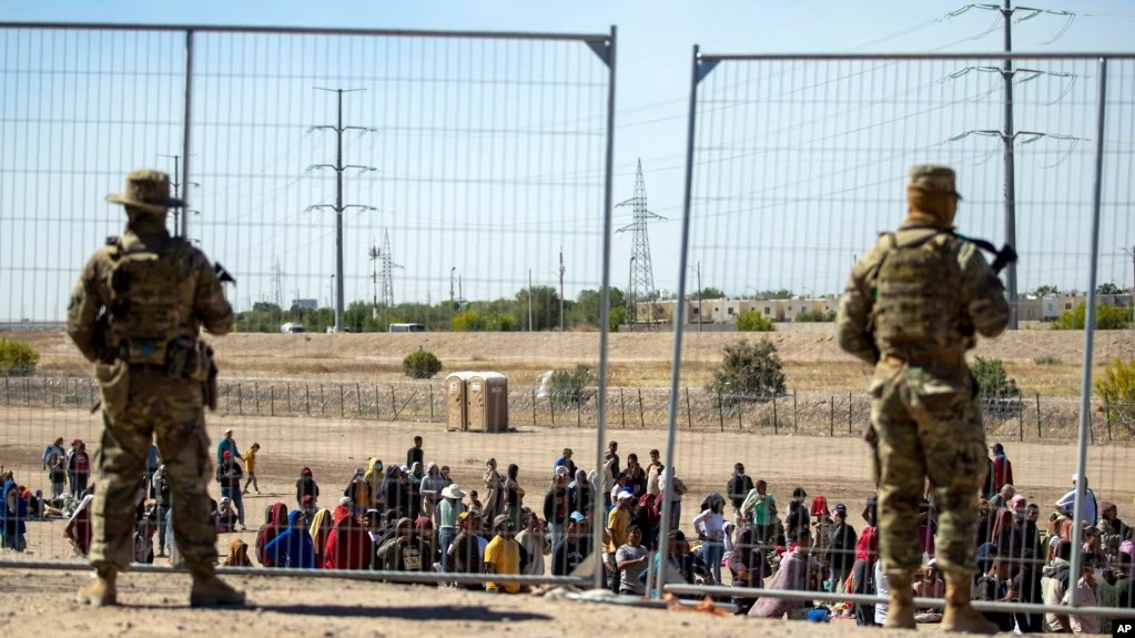 Migrantes esperan en fila junto a la valla fronteriza bajo la vigilancia de la Guardia Nacional de Texas para ingresar a El Paso, Texas. Foto: fuente externa.