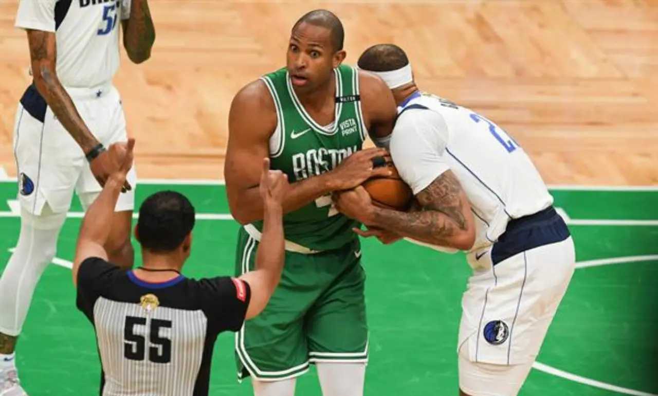 El centro de los Boston Celtics, Al Horford (C), y el de los Dallas Mavericks, Daniel Gafford (d), agarran un balón suelto mientras el árbitro Bill Kennedy pide