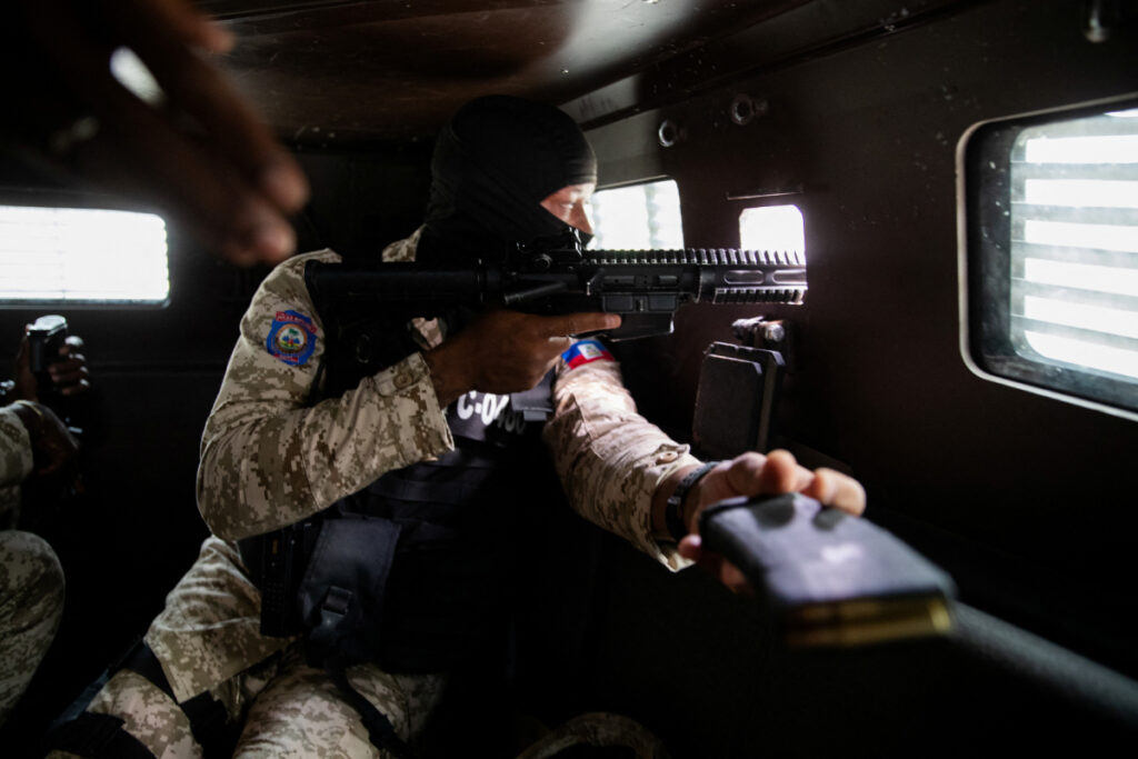 Un agente de policía haitiano apunta con su arma por la ventana de un vehículo blindado durante una patrulla en el centro de Puerto Príncipe el 16 de enero de 2026.
